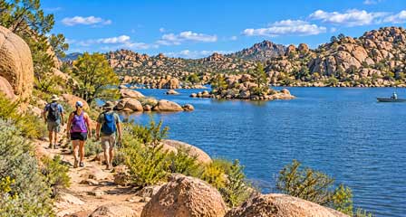 Three hikers on a rocky trail overlooking Watson Lake and the Granite Dells near Prescott, Arizona