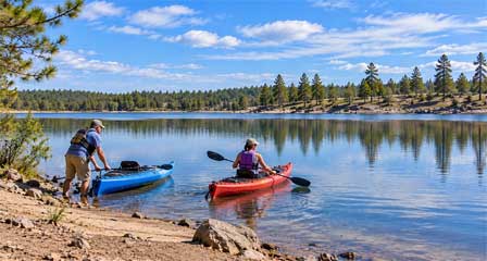 Two kayakers launching blue and red kayaks from the rocky shoreline of Willow Springs Lake Arizona